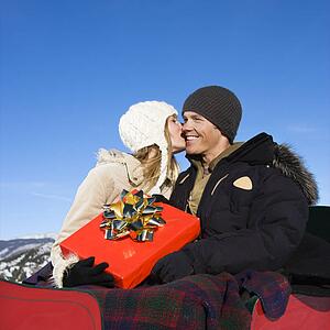 Woman kissing cheek of man in a sleigh in winter.