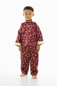 Asian boy standing against white background in traditional attire.