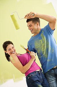 Couple standing in front of partially painted wall playfully putting paint on each other