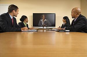 Businesspeople sitting at conference table looking at flat screen display.