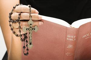 Woman holding Holy Bible open with rosary and crucifix in hand
