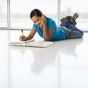 Girl lying on floor doing homework while talking on cell phone