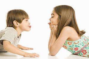 Portrait of girl and boy lying looking at eachother sticking out tongues.