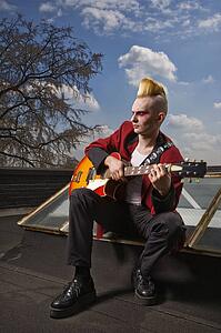 Male punk sitting on a skylight playing guitar