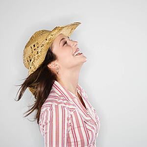 Profile of young woman wearing cowboy hat smiling with wind blowing hair.