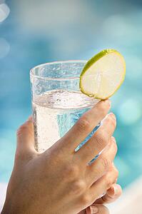 Woman's hands holding drink glass garnished with lime slice next to pool