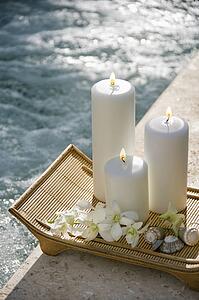 Lit pillar candles on tray with white orchids beside pool