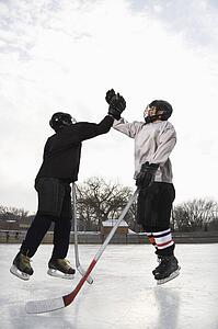 Two boys in ice hockey uniforms giving each other high five on ice rink