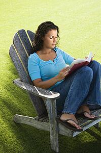 Portrait of pretty young adult brunette female sitting in chair reading book.