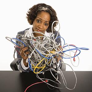 Businesswoman holding bundle of tangled computer cords with overwhelmed look on her face.