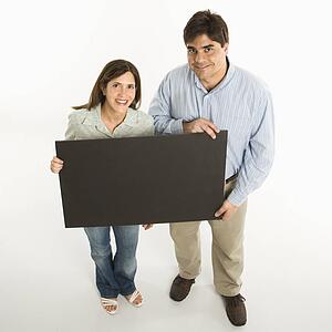 Couple standing smiling holding blank sign against white background