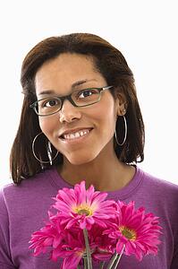 Woman wearing glasses holding pink flowers and smiling at viewer
