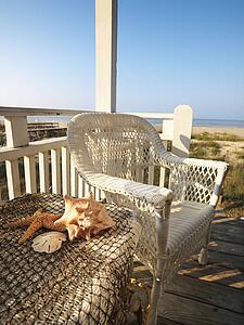 Still life shot of a wicker chair and sea shells on table with beach in background.