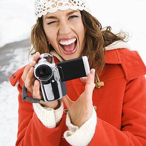 Young adult female in winter clothing pointing digital camera at viewer and winking