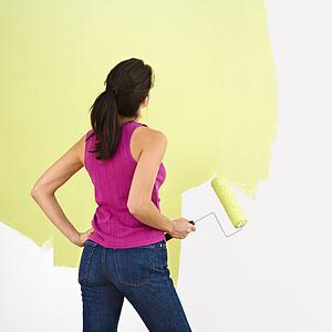 Woman standing and looking at partially painted wall holding paint roller