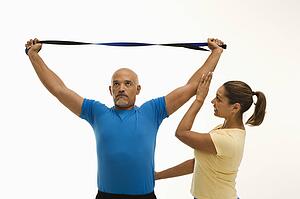 Mid adult multiethnic woman assisting mid adult multiethnic man with stretching band.