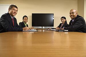 Businesspeople sitting at conference table smiling with flat screen tv