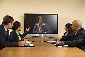 Businesspeople sitting at conference table looking at flat screen display.