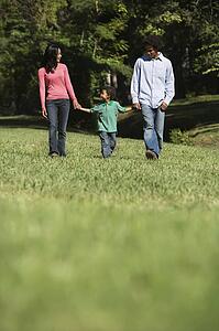 Parents and young son walking in park holding hands.