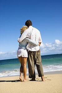 Attractive couple standing embracing looking out at ocean in Maui, Hawaii.