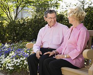 Mature Caucasian couple sitting on bench looking at each other.