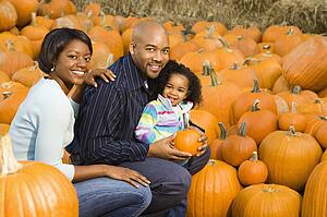 Parents and daughter picking out pumpkin and smiling at outdoor market
