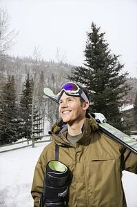 Winter clothing walking in snow carrying ski equipment and smiling