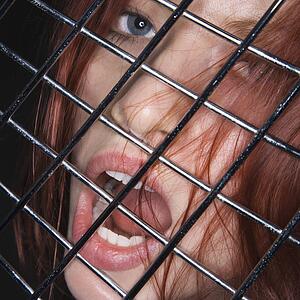Woman with mouth open behind metal fence.