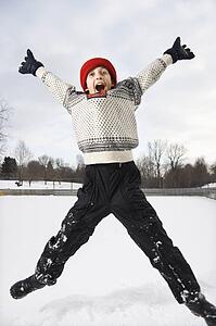 Excited Caucasian boy wearing sweater and red winter cap jumping in air with arms and legs outstretched.