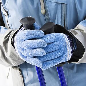 Close up of female skier hands wearing blue gloves holding ski poles.