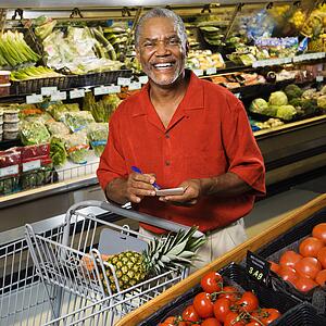 Middle aged African American man in grocery store holding shopping list and smiling at viewer.