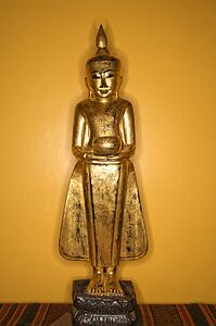 Golden wooden Buddha statue from Myanmar against yellow wall.