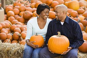 Couple sitting on hay bales holding pumpkins
