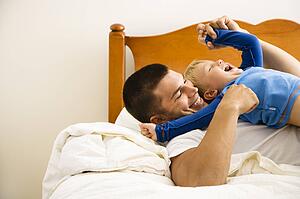 Caucasian toddler boy and father playing and tickling in bed.