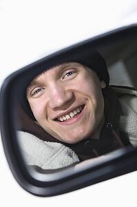 Caucasian male teenager looking at himself in side view mirror of car.
