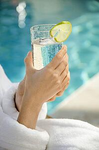 Woman's hands holding beverage glass garnished with lime slice next to pool