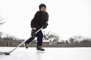 Boy in ice hockey uniform skating on ice rink moving puck.