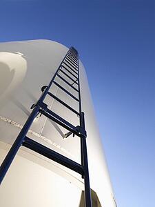 Low angle view of metal grain storage silo with ladder assending to top.