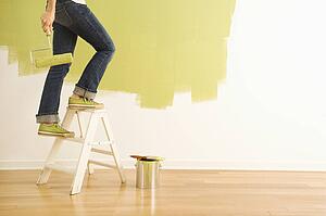 Legs of woman climbing stepladder holding paint roller.