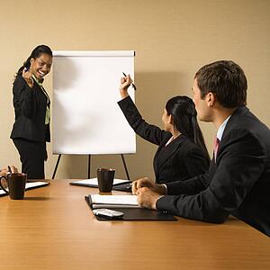 Businesspeople sitting at conference table while businesswoman gives presentation.
