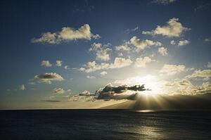Pacific ocean and island with sun streaming through clouds.
