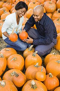 Couple picking out pumpkins and smiling at outdoor market.