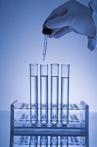 Hand holding dropper over test tubes.