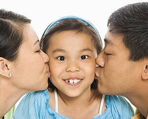 Mother and father kissing opposite cheeks of daughter