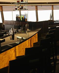 Empty bar in restaurant with row of barstools and windows in background. 
