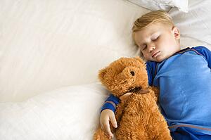 Toddler boy sleeping in bed with teddy bear