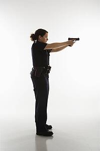 Side view of mid adult Caucasian policewoman standing and aiming handgun.