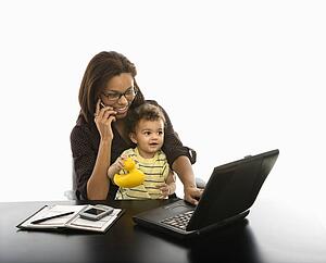 Mid adult businesswoman working on laptop and cell phone with toddler son on lap