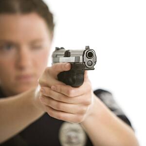 Close up of mid adult female Caucasian law enforcement officer aiming gun at viewer with one eye closed.