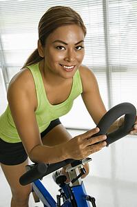 Mid adult woman pedaling exercise bicycle smiling at viewer.